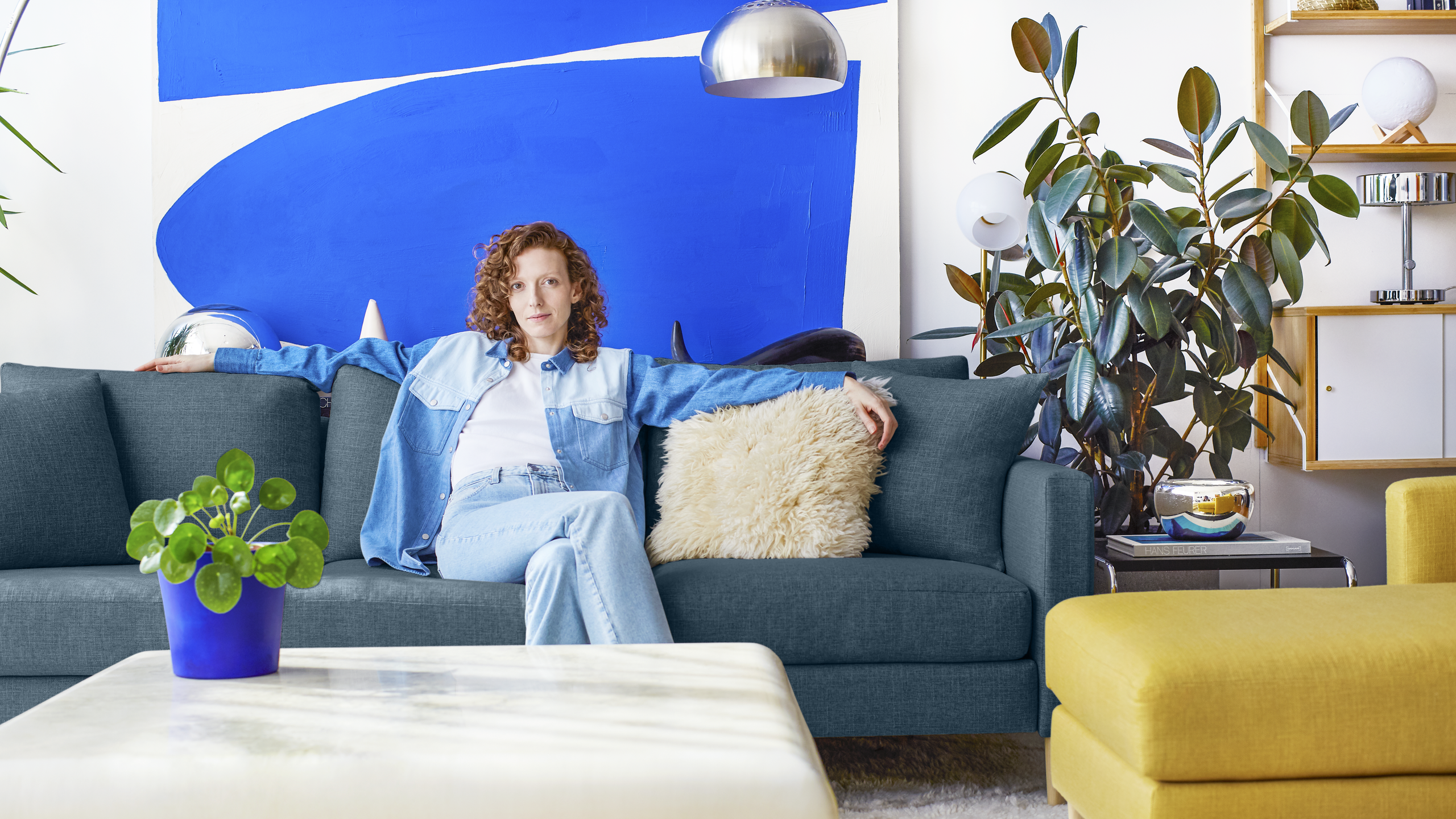 Woman sitting on teal sofa with white ottoman